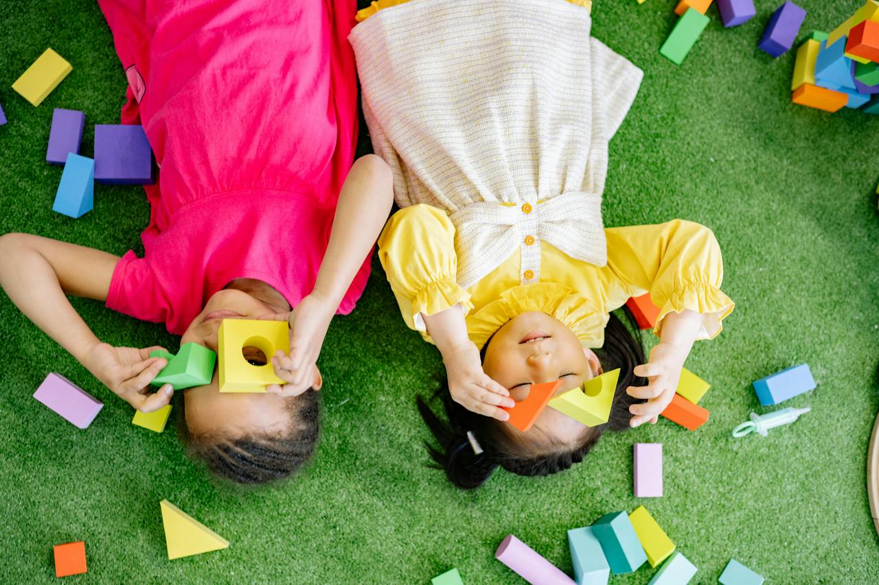 "Two children laying on a green carpet and play with blocks"